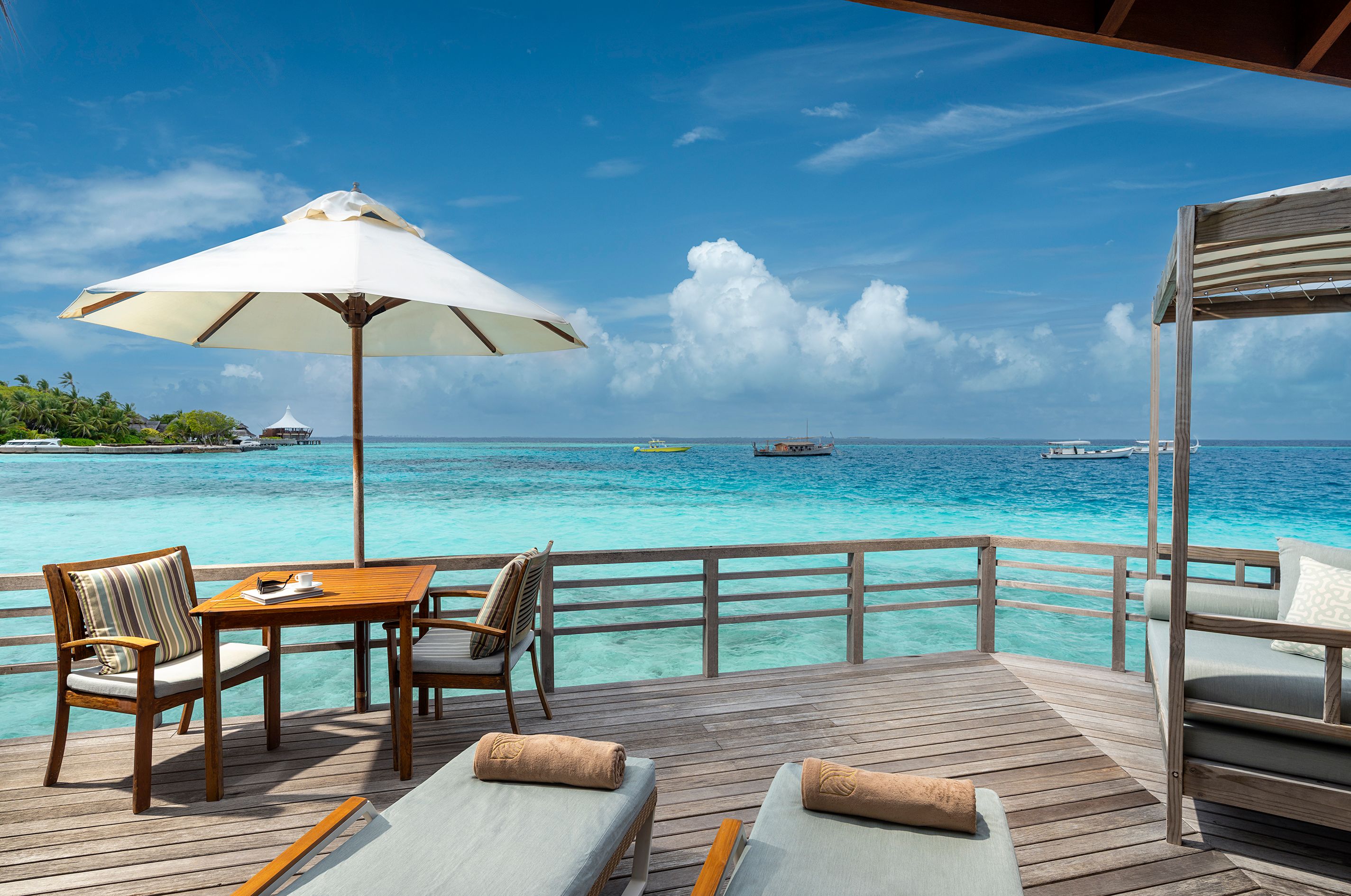 Water Villa deck with a dining table, sun loungers and parasol over the lagoon