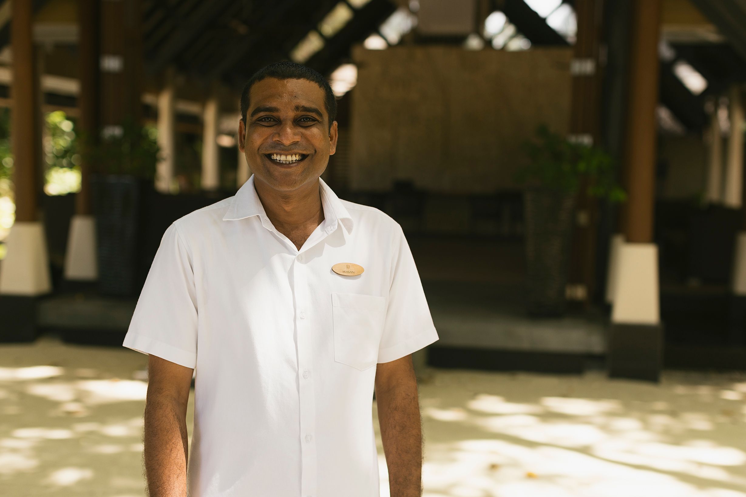 A smiling Baros team member in a white shirt standing in front of the Welcome Pavilion