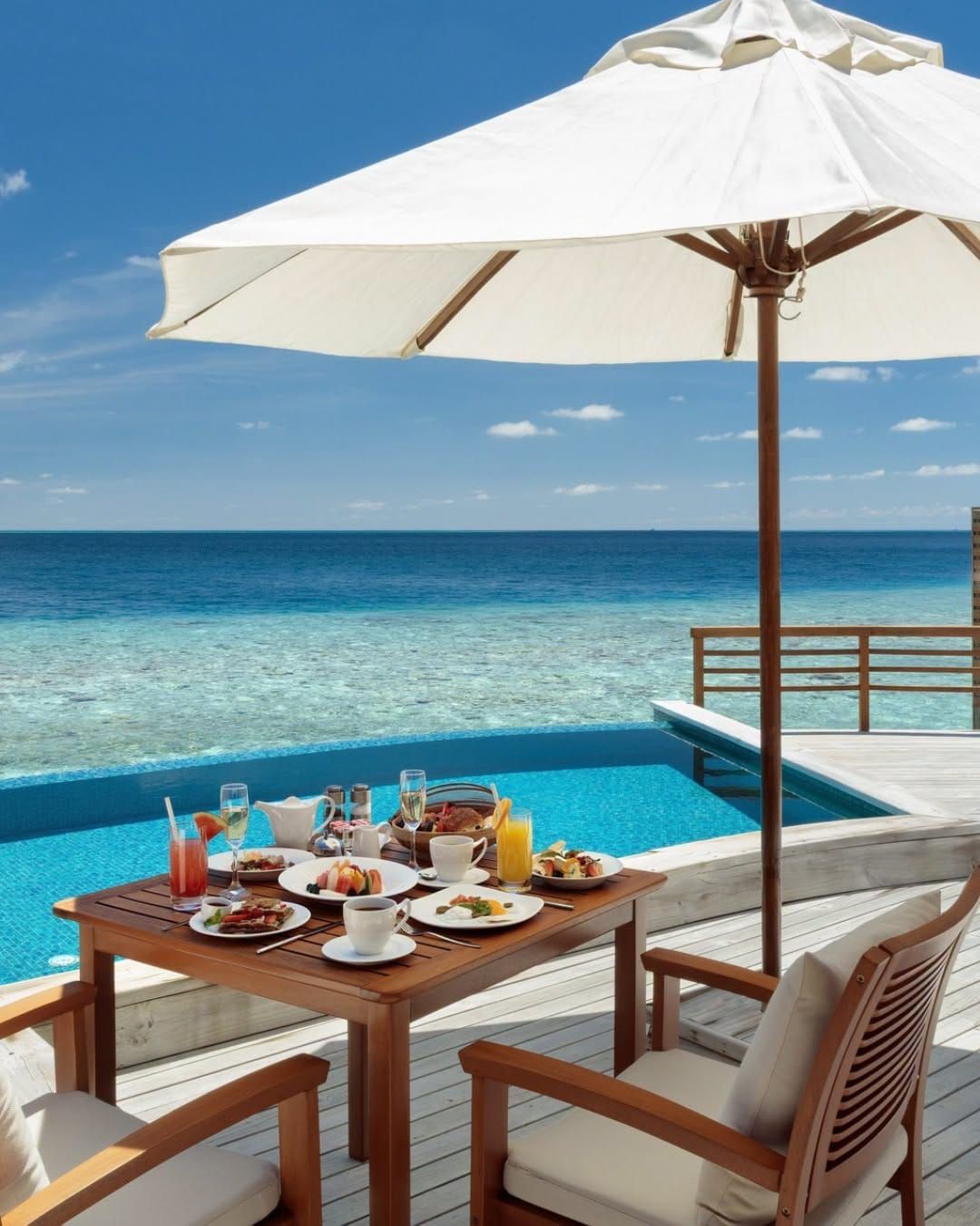 Breakfast table set beside an overwater villa pool under a white parasol