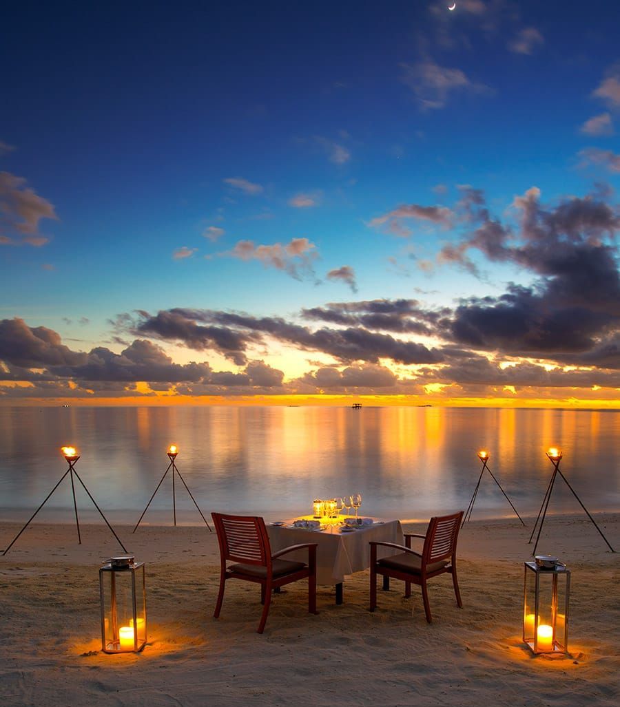 Candlelit table for two on the beach under a glowing sunset sky