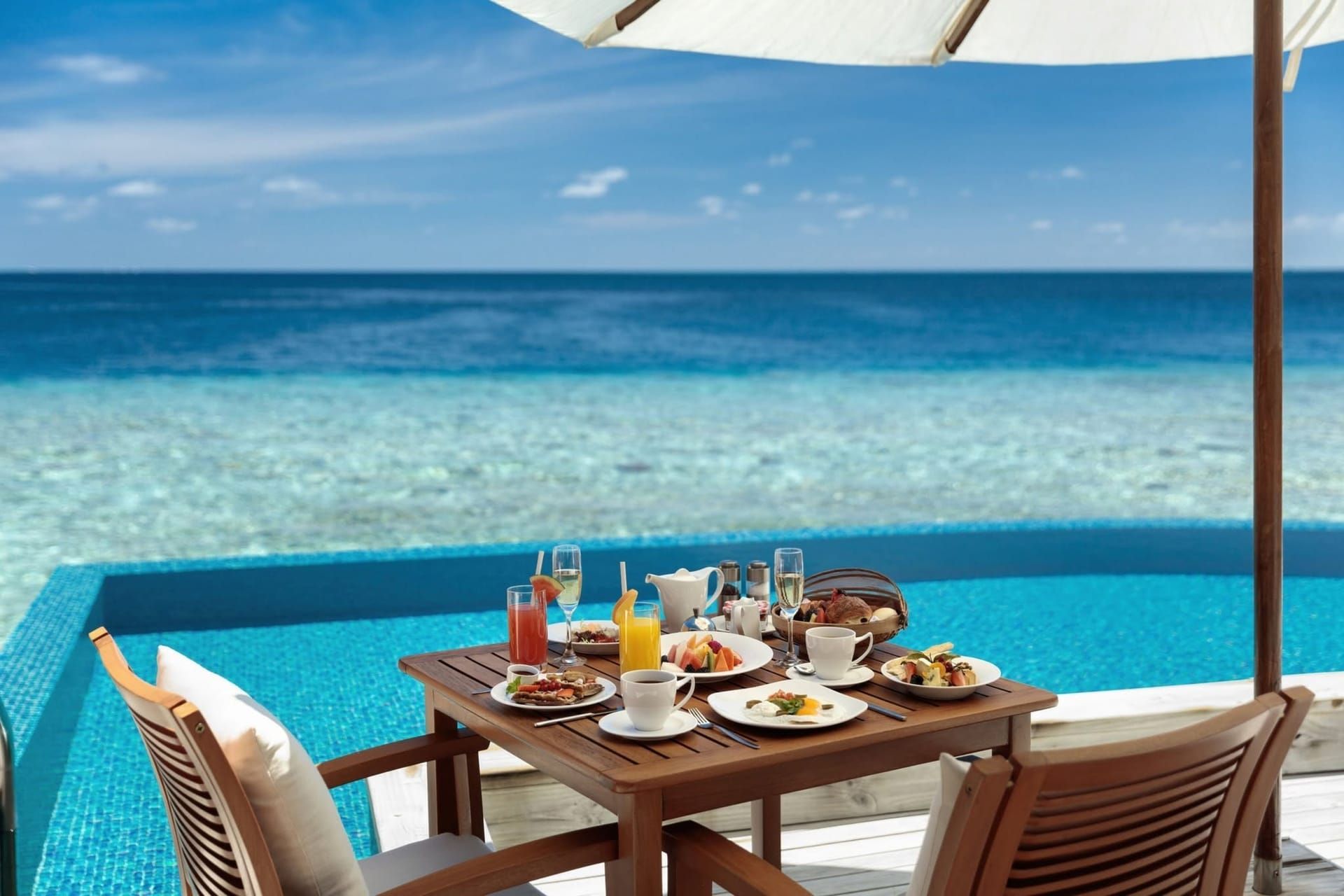Breakfast spread on a table beside an overwater pool facing the ocean