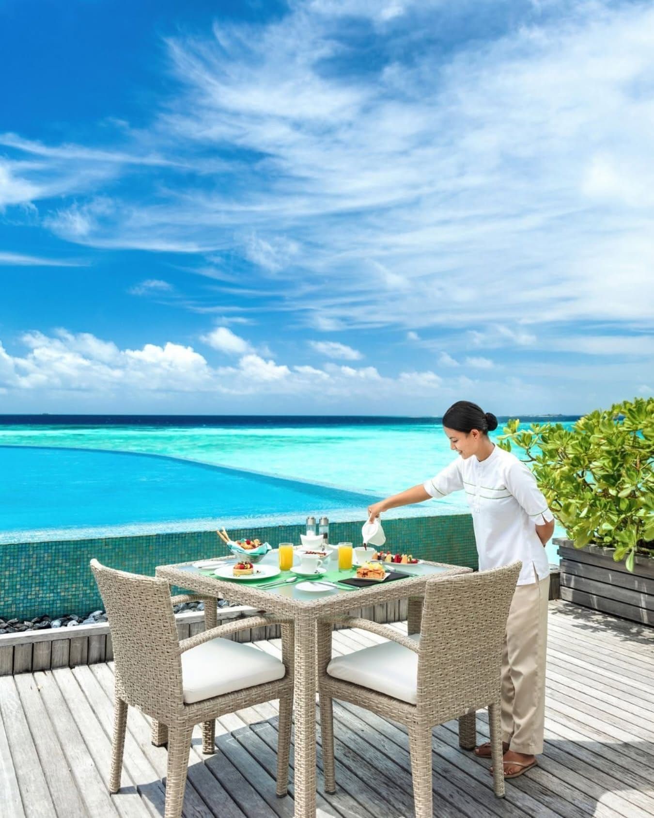 Server setting a breakfast table on an overwater deck under blue sky