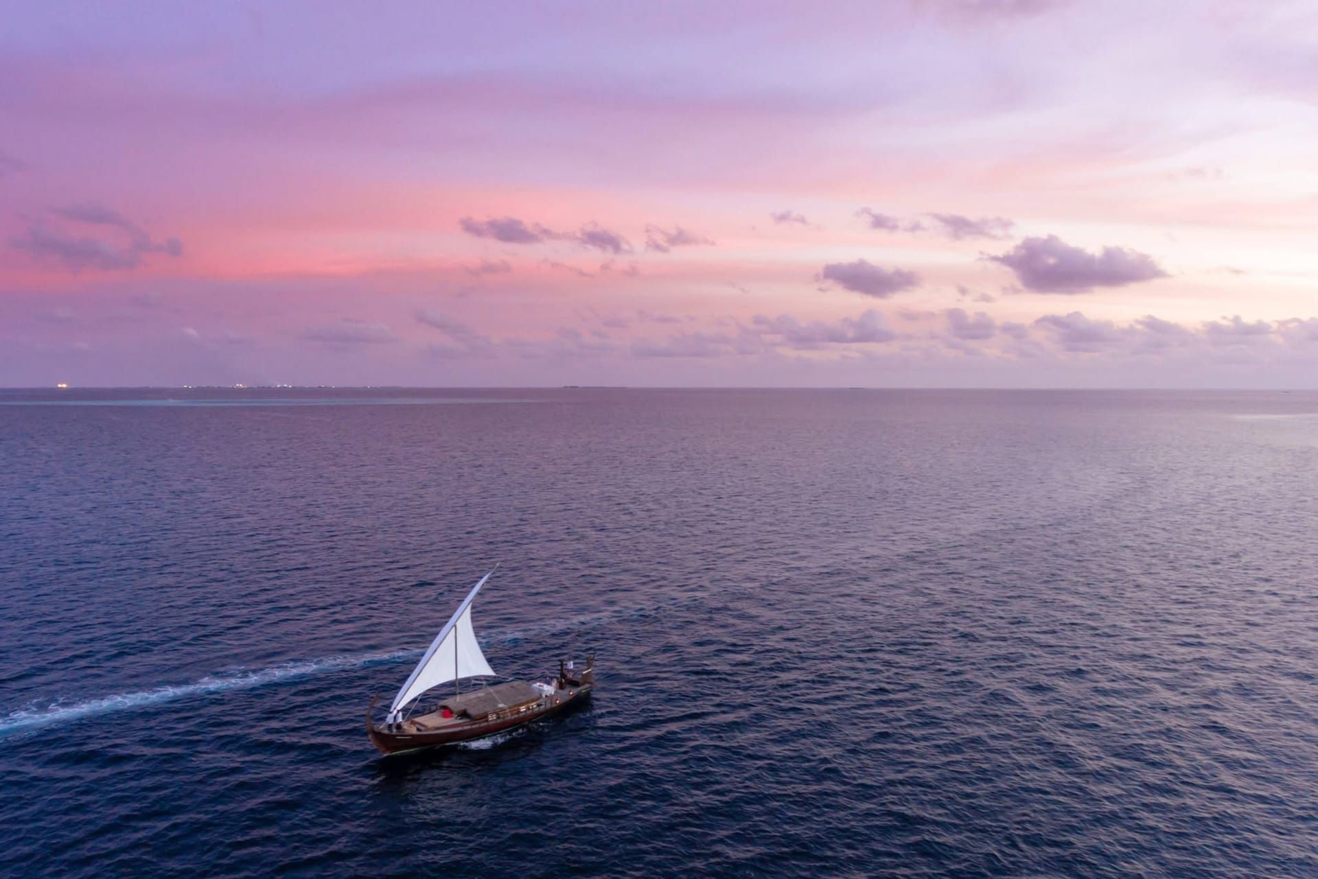 Aerial view of a dhoni sailing on calm water under a pink sunset sky