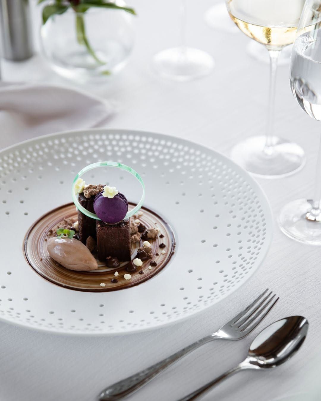 Plated chocolate dessert under a glass dome on a white table