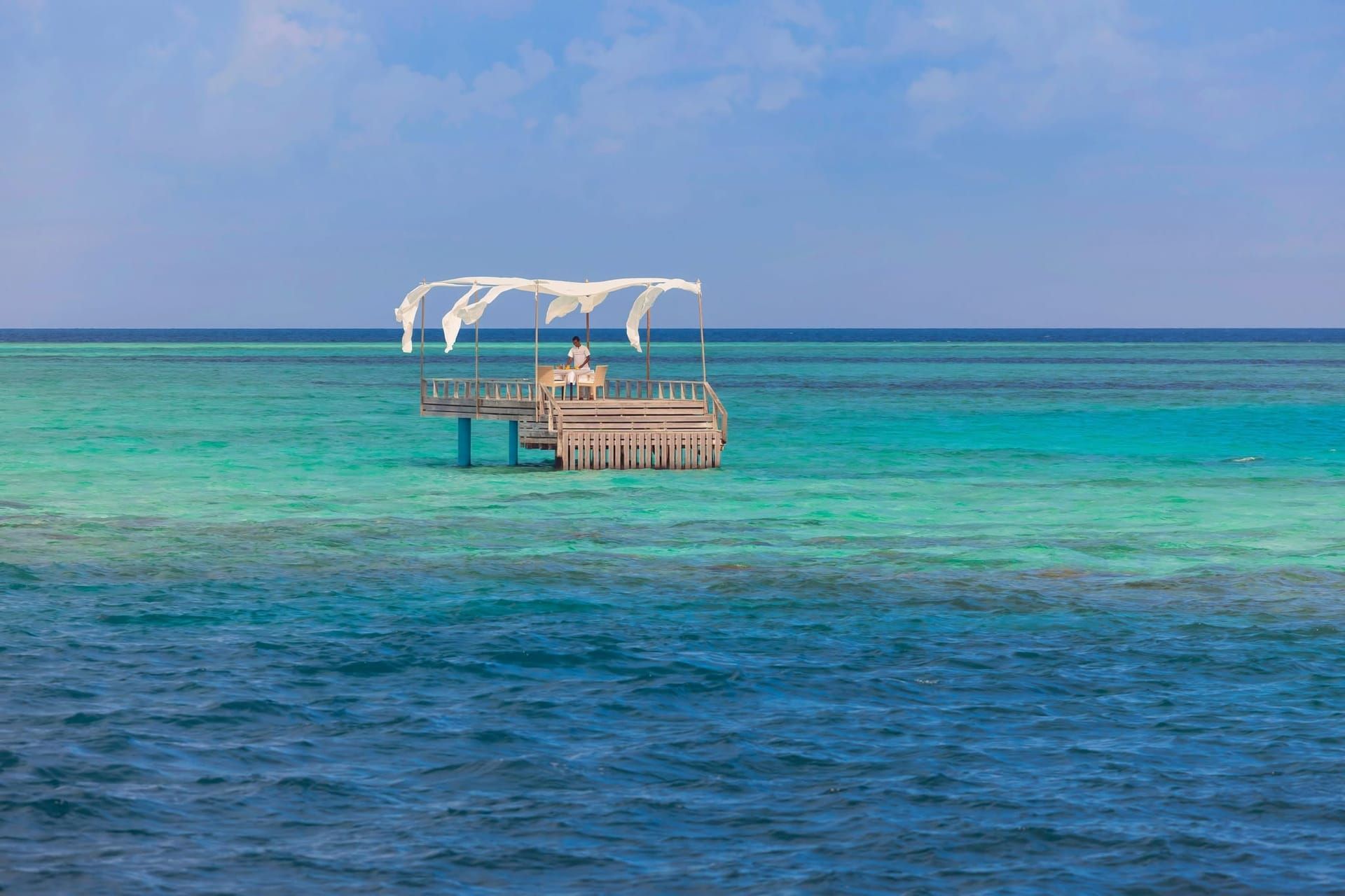 Canopied dining deck on stilts in the middle of a turquoise lagoon