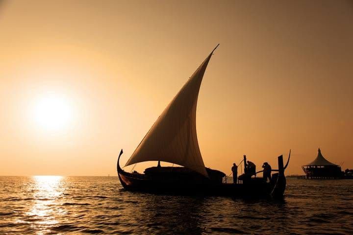 Silhouette of a dhoni under sail with the sun low over the sea