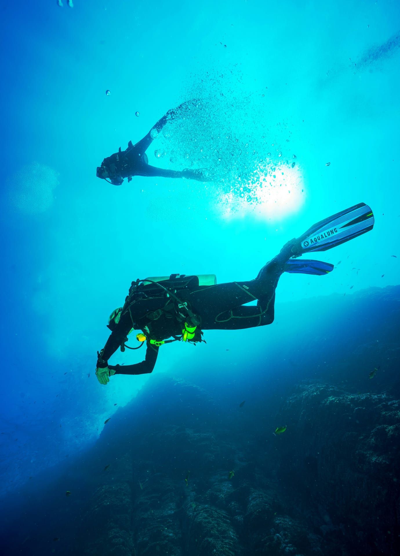 Two scuba divers silhouetted against sunlight filtering into deep blue water
