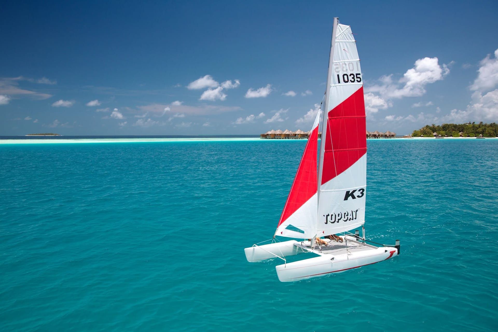 Catamaran with a red and white sail on a turquoise lagoon