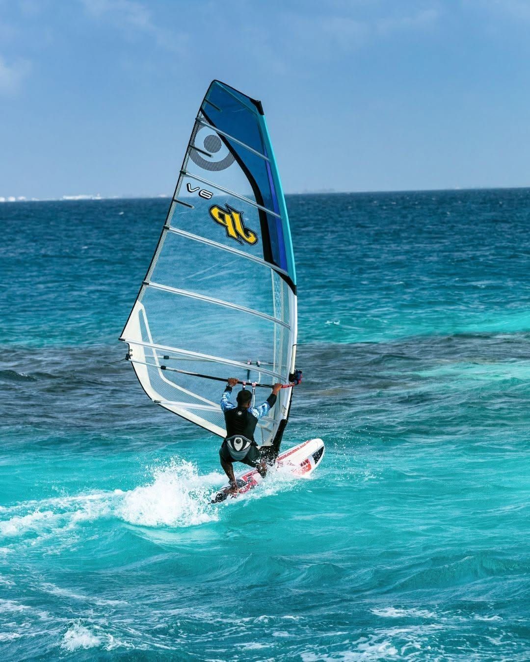 Windsurfer with a blue sail skimming across turquoise water
