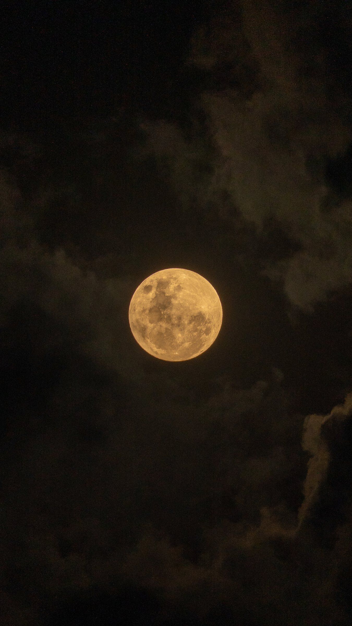A full moon rising through the clouds