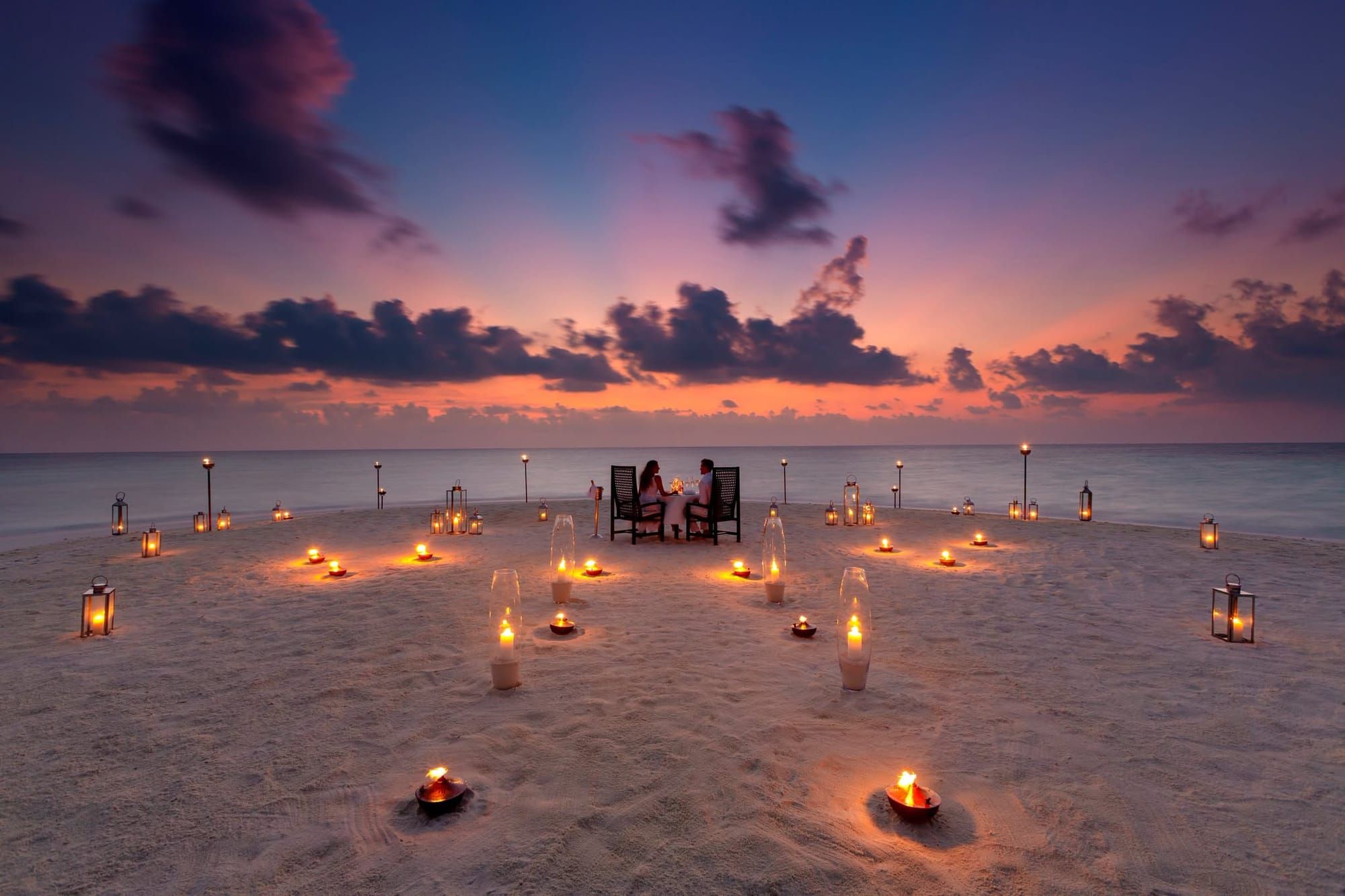Private candlelit dinner on a sandbank ringed by lanterns at sunset
