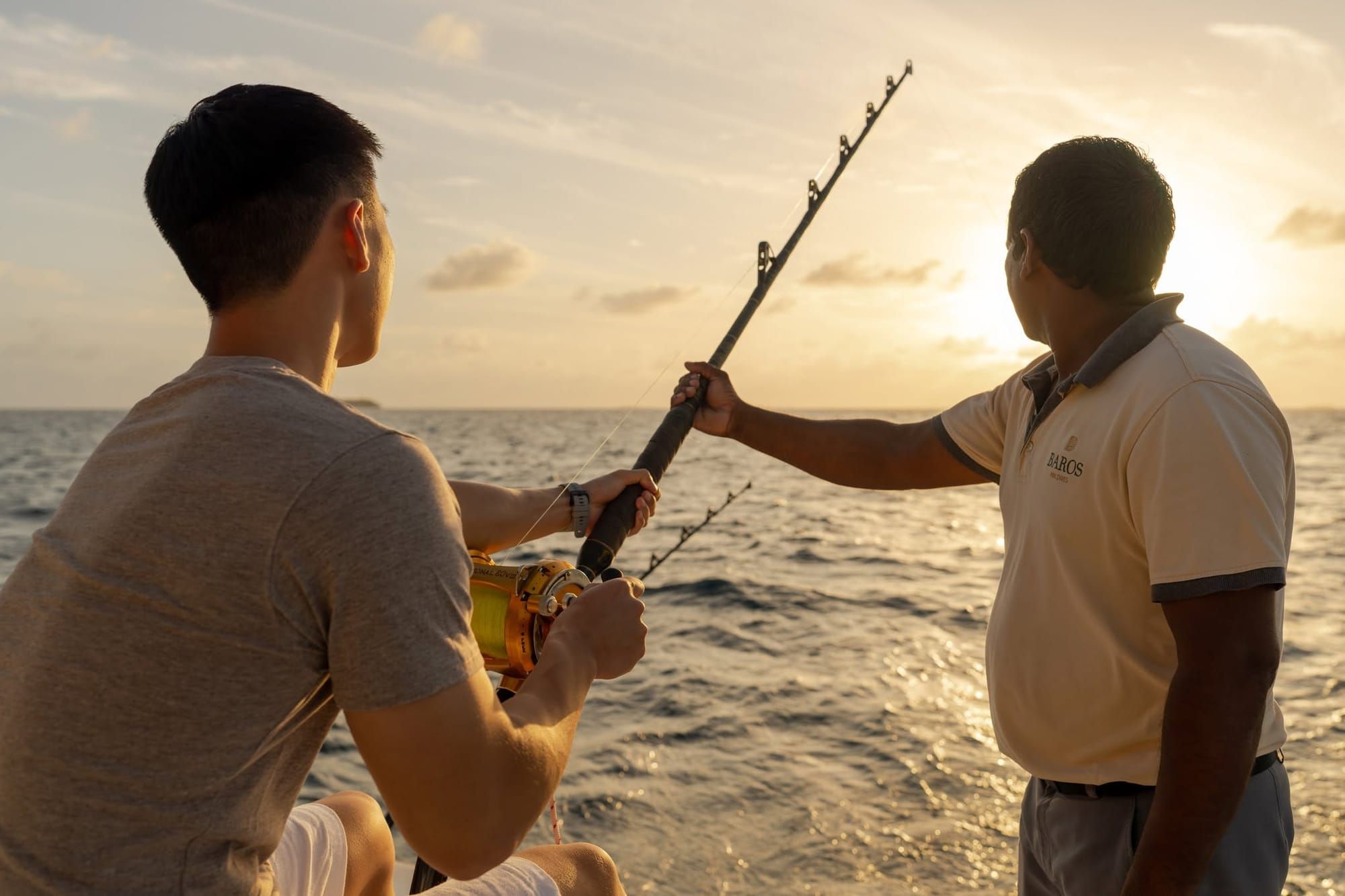 Guest and staff member fishing from a boat at sunset
