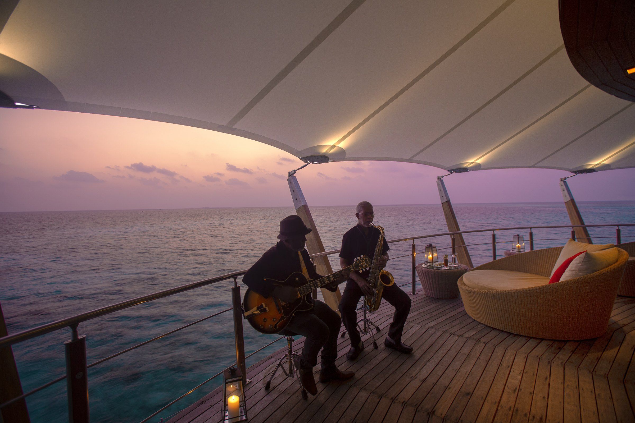 Two musicians playing guitar and saxophone on the Lighthouse Lounge deck at dusk