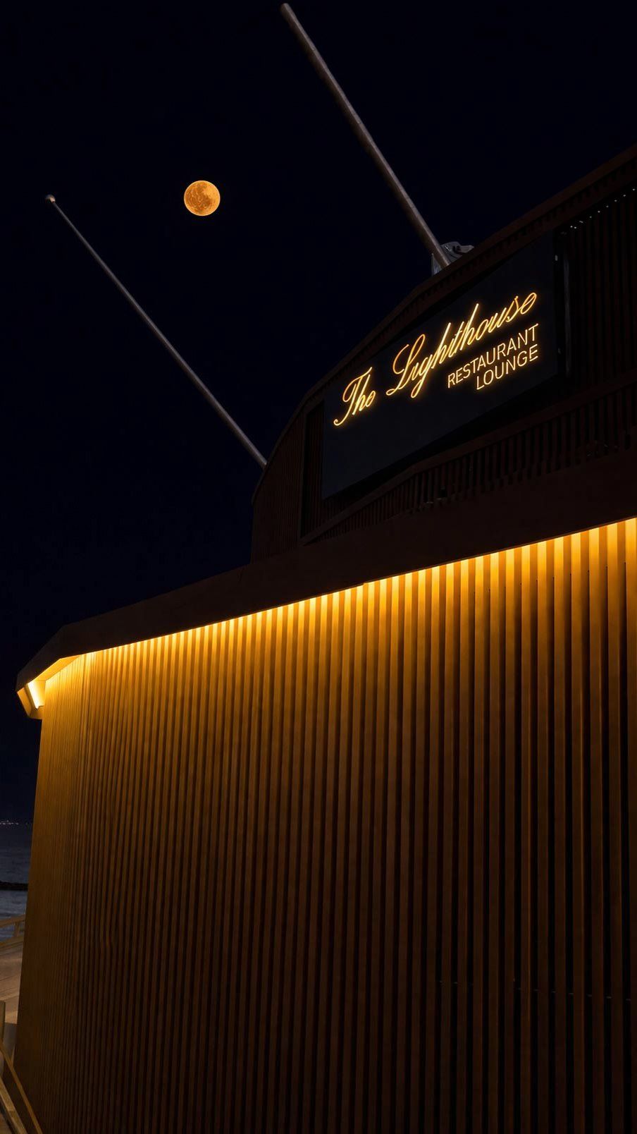The Lighthouse Restaurant & Lounge sign glowing beneath a rising full moon