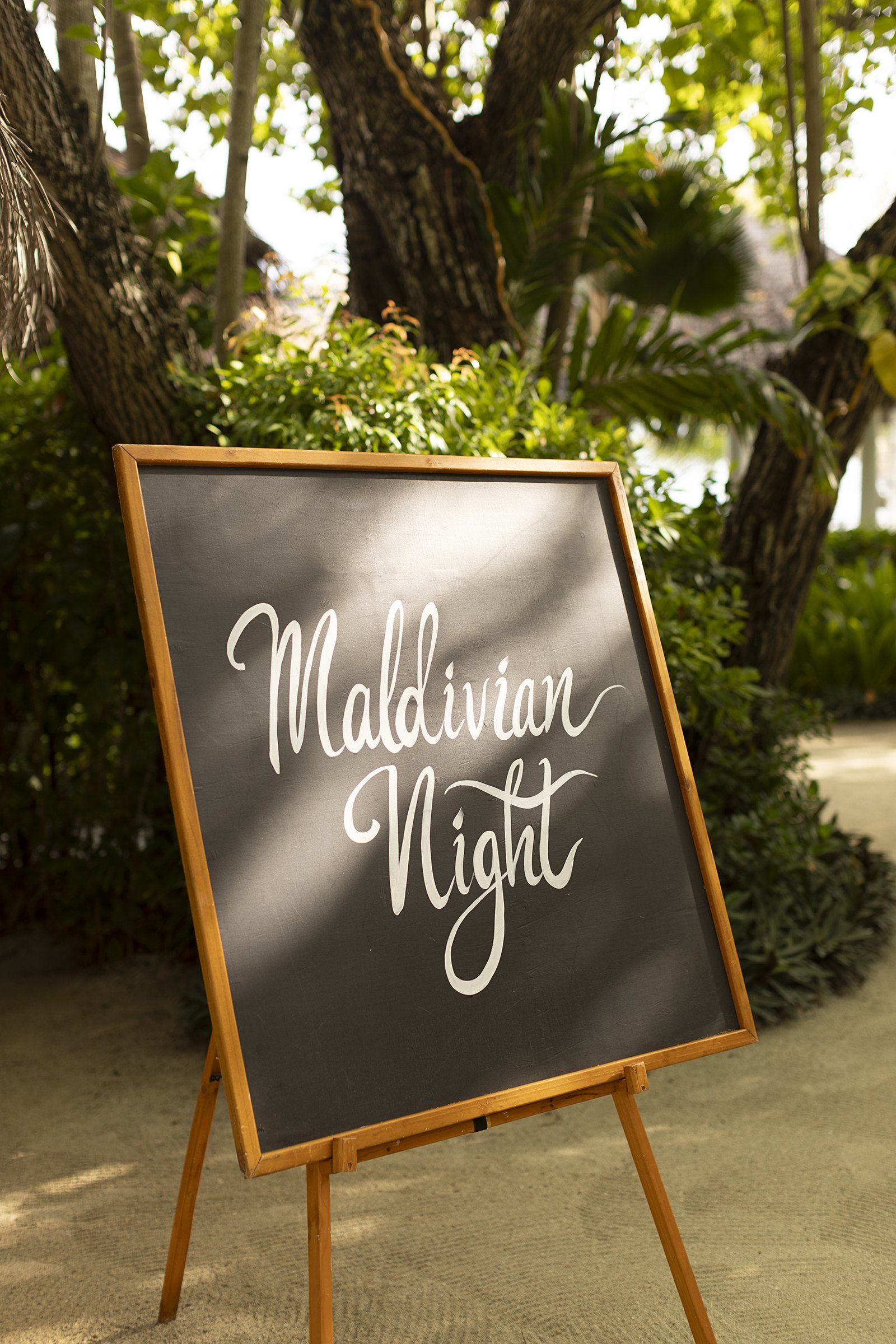 A chalkboard sign reading Maldivian Night in a tropical garden