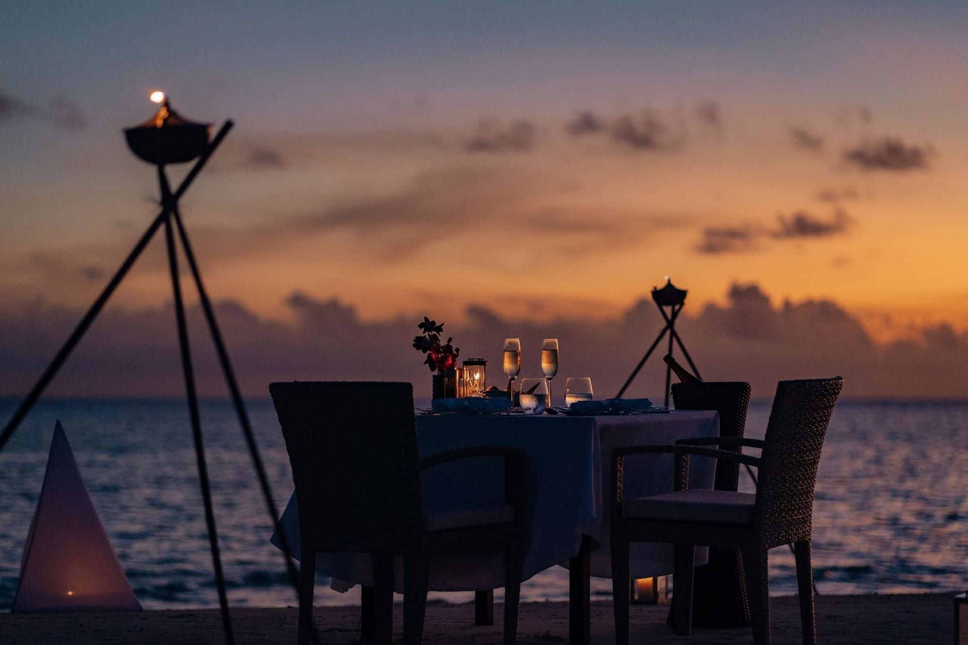 Candlelit dinner table for two on the beach at sunset beside tiki torches