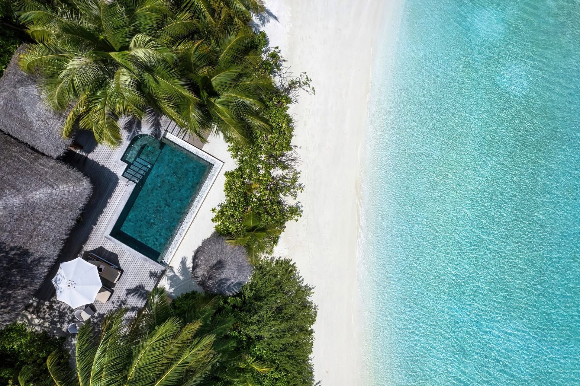 Aerial view of a thatched beach villa with private pool beside white sand and lagoon