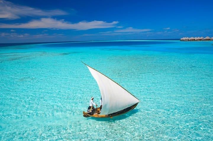 Traditional dhoni with a white sail gliding across a shallow turquoise lagoon