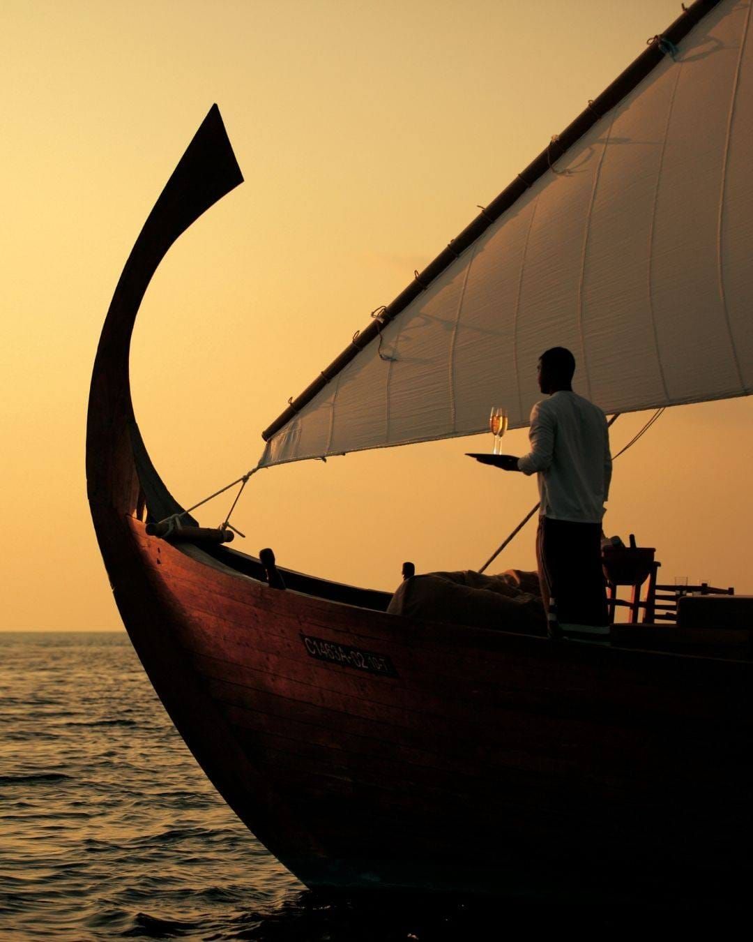 Silhouette of a traditional dhoni with a crew member against a golden sunset