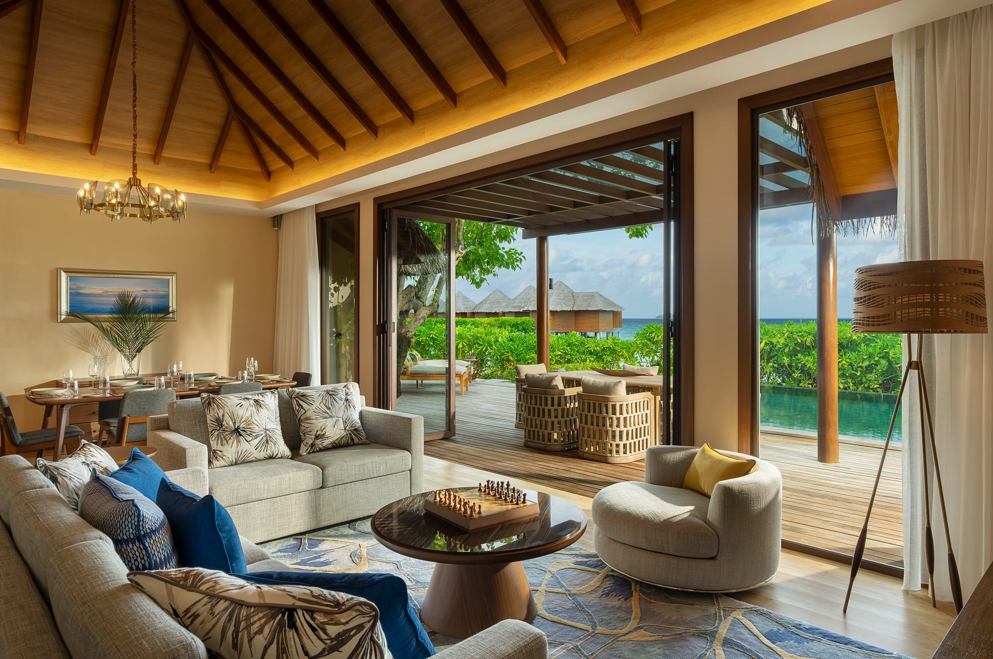 Spacious villa living room with sofas and timber ceiling opening to a lagoon deck