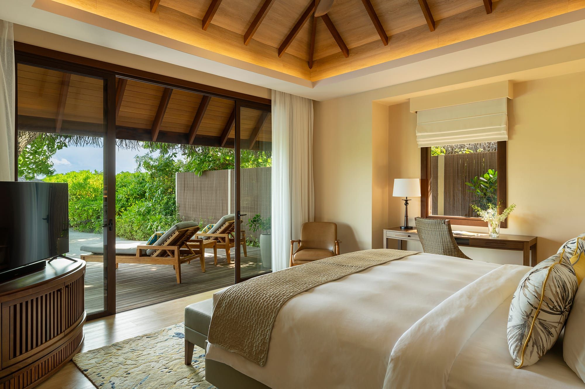 Villa bedroom with double bed and glass doors opening onto a garden deck
