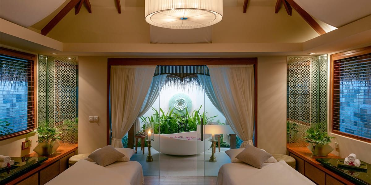 Spa treatment room with two beds facing an open window with greenery