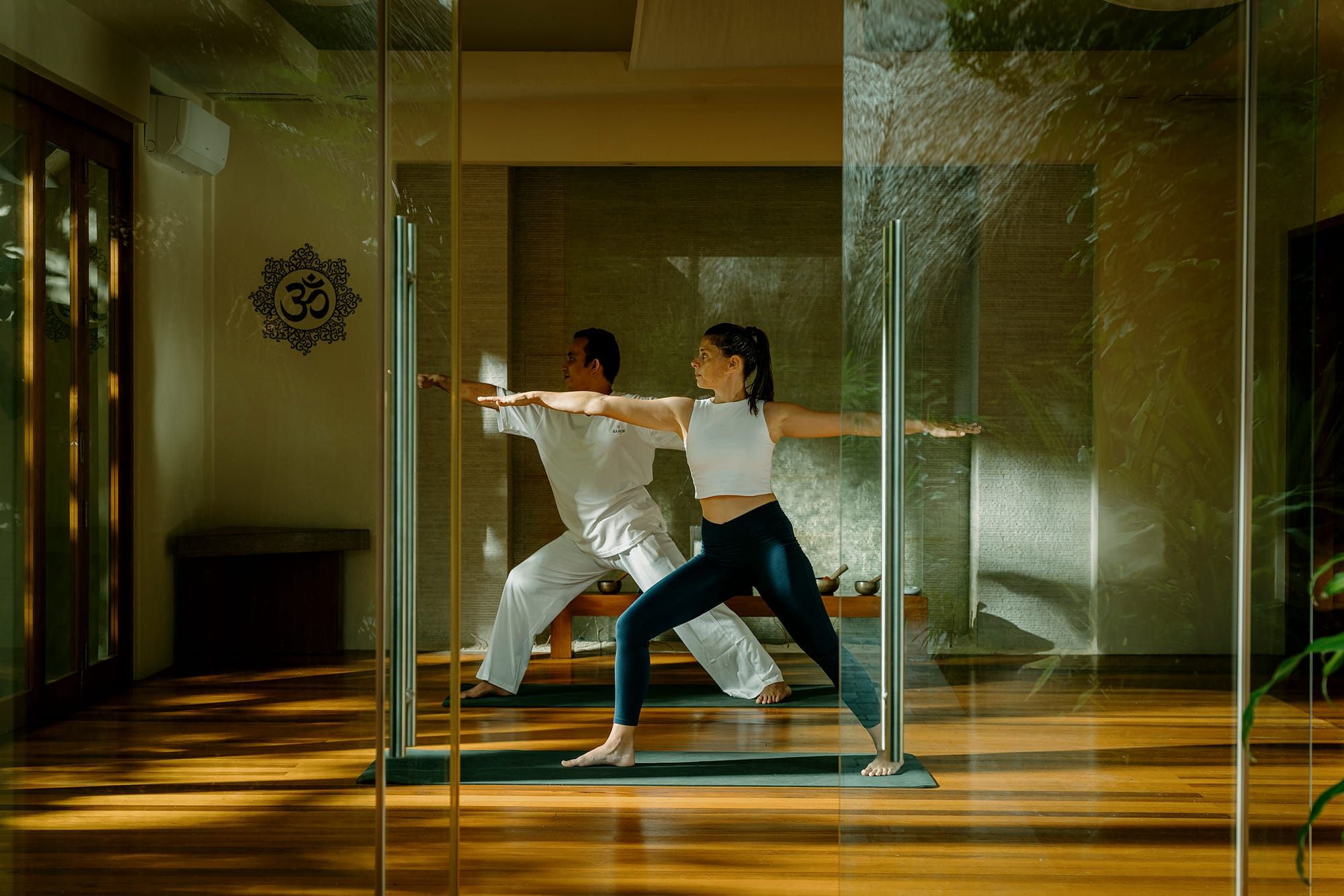 Two people practising a yoga warrior pose in a glass-walled studio