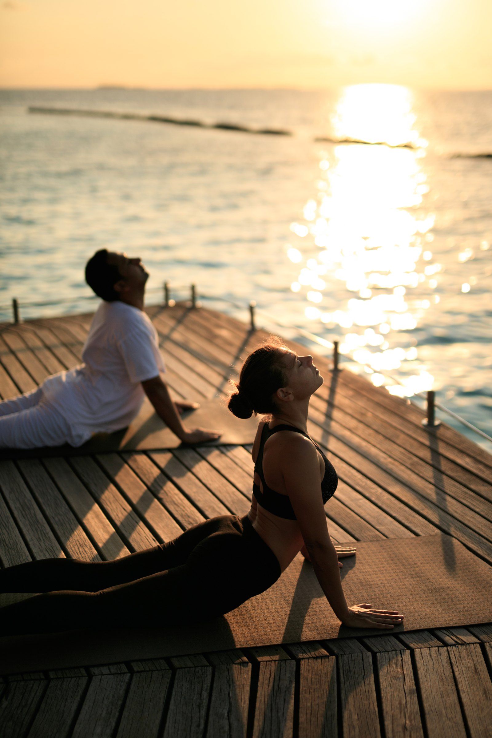 Two guests practising sunrise yoga on the Lighthouse Lounge deck above the sea
