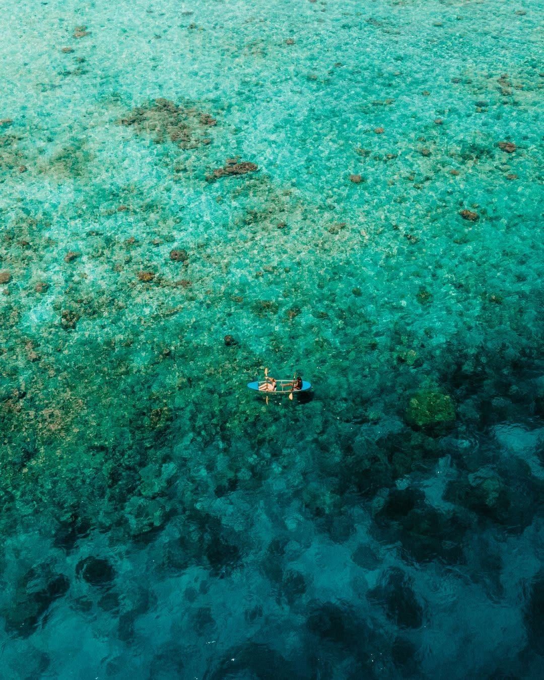 Aerial view of a lone snorkeller floating above a turquoise reef