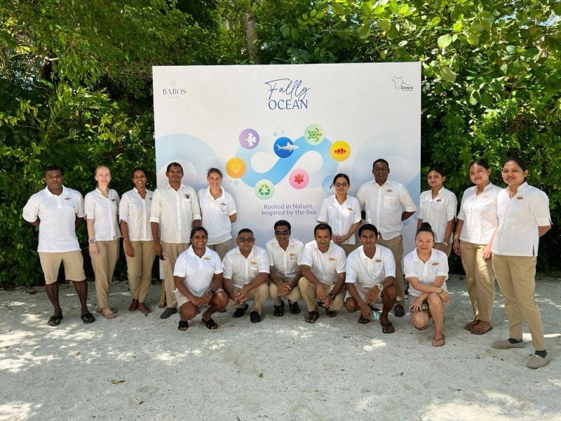 Group of staff in white uniforms posing in front of an ocean-themed banner