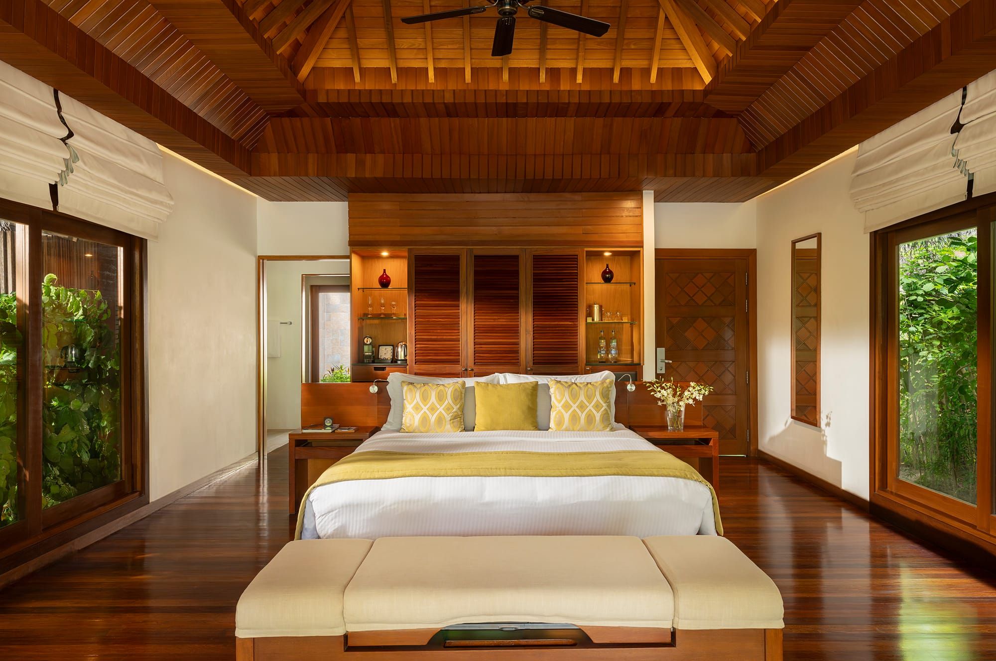 Symmetrical villa bedroom with timber ceiling, double bed and bench