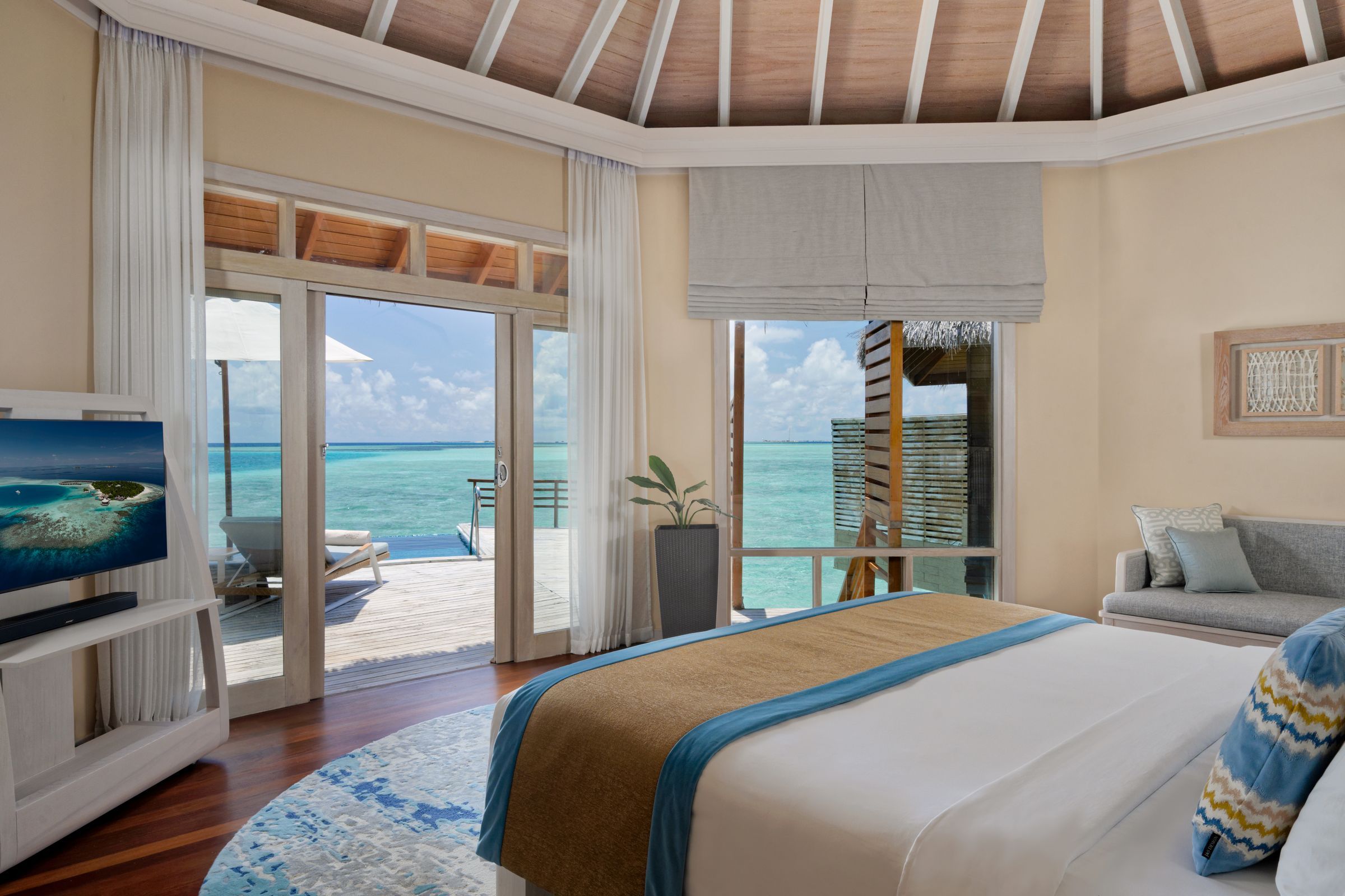 Bedroom of a Water Pool Villa, with glass doors open to the lagoon