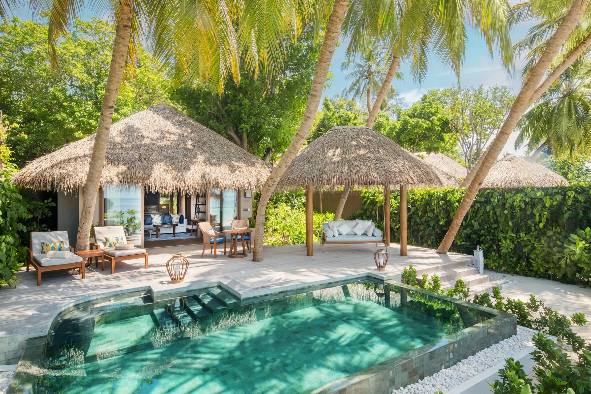 Beach villa garden with a private pool framed by thatched pavilions and palms