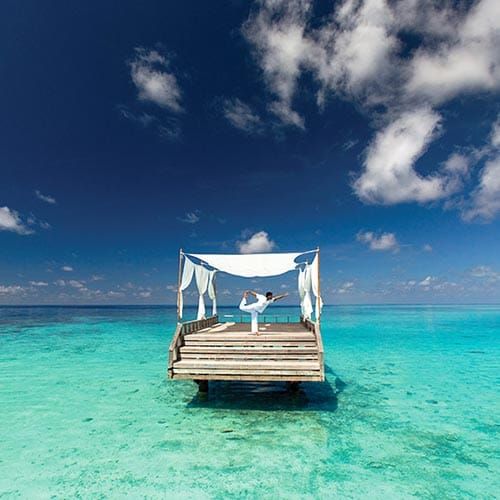 Person doing yoga on a canopied deck in the middle of a turquoise lagoon