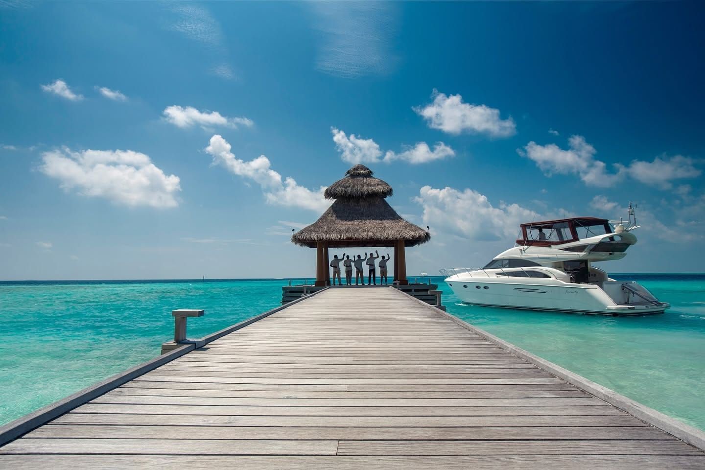 Long timber jetty leading to a thatched pavilion with a yacht moored alongside